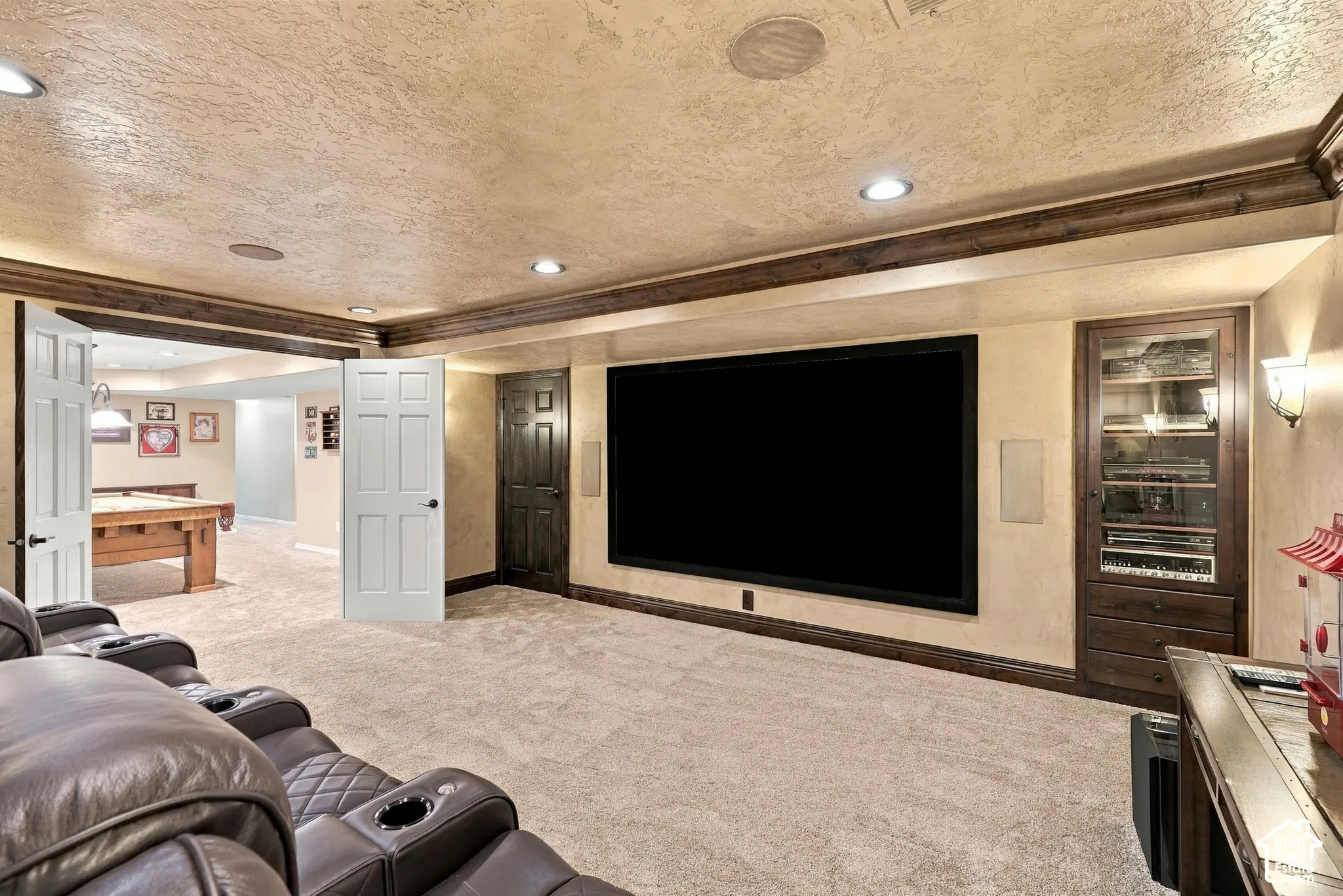 Large screen display, built-in entertainment cabinetry with glass-front display, ceiling-mounted speakers, recessed lighting, and wood-finish ceiling beams
