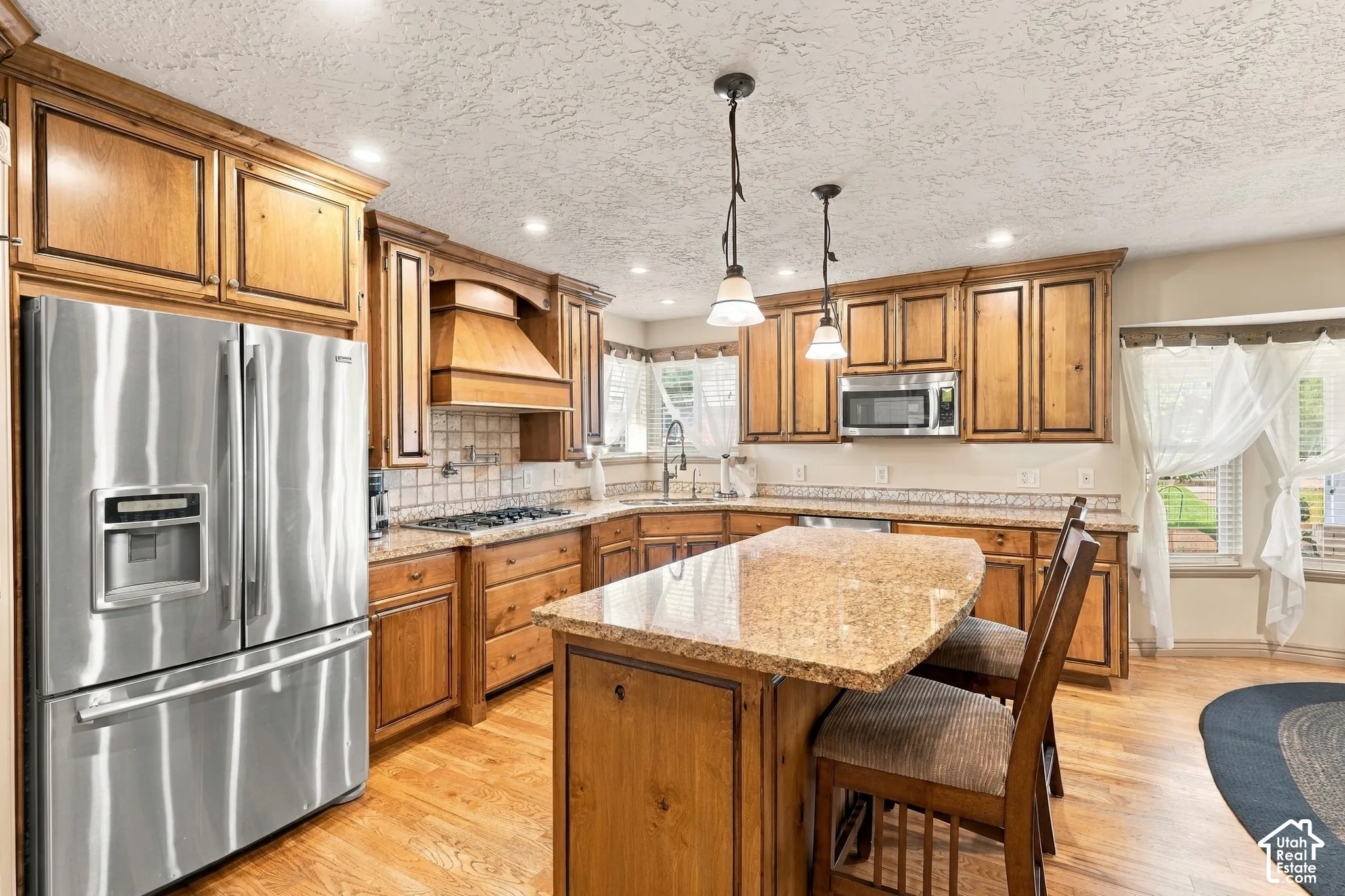 Wood-finish cabinetry with crown molding, stainless steel appliances, a kitchen island with seating, pendant lighting, and wood-finish flooring
