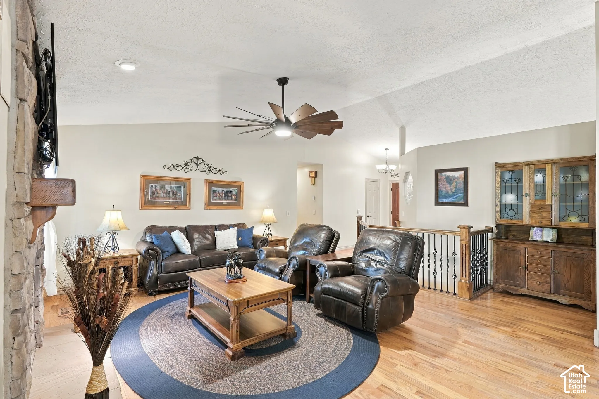Vaulted ceiling, stone-clad fireplace, wood-finish flooring, recessed lighting, and a decorative railing with wrought iron balusters