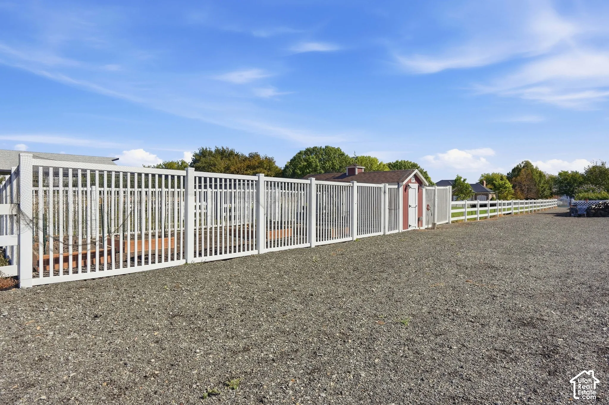Gravel lot with white fencing and a red utility shed