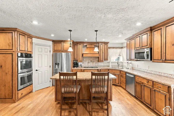 Wood-finish cabinetry, stainless steel double wall ovens, wood-finish flooring, central island with seating, and recessed lighting