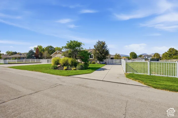 Expansive front yard with manicured lawn, white picket fencing, and a concrete driveway