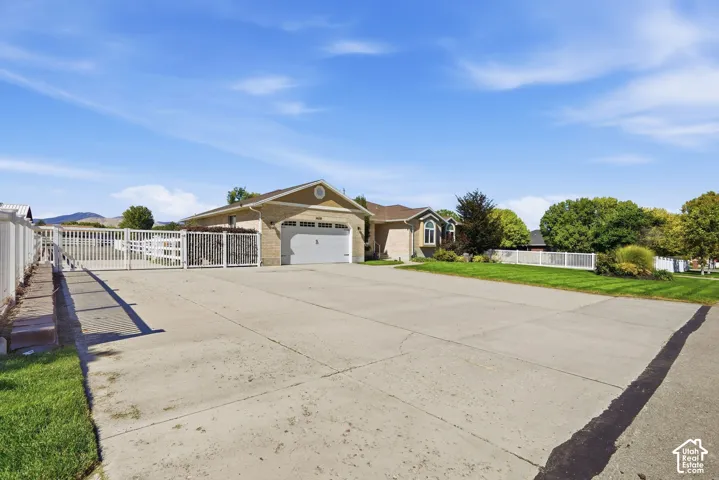 Brick exterior with an attached garage, featuring a concrete driveway and white fencing