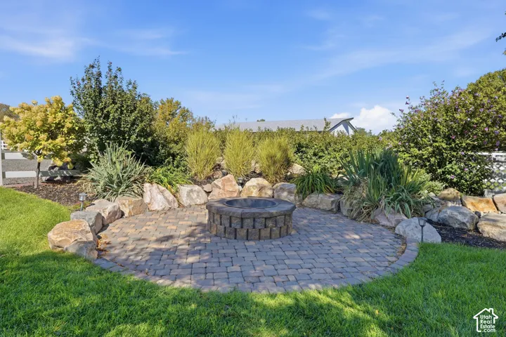 Paver patio with a stone fire pit, surrounded by lush landscaping and decorative boulders