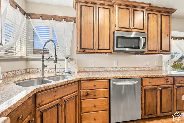 Wood-finish cabinetry with crown molding, stainless steel microwave, dual basin undermount sink, and durable stone-look countertops