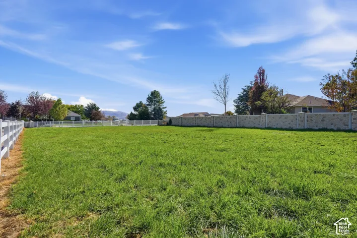 Expansive parcel featuring a grassy field, white perimeter fencing, and a decorative stone wall