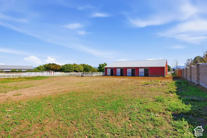 Red barn structure with a metal roof, multiple sliding doors, white fencing, and a concrete-block privacy wall