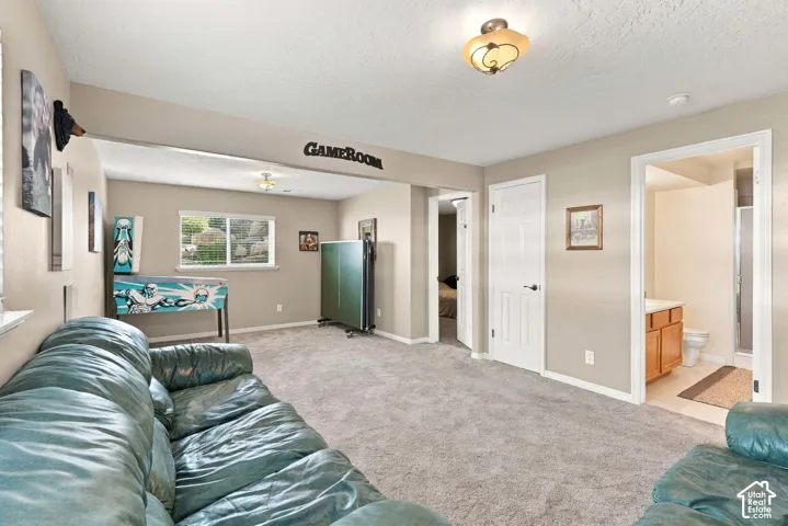 Carpeted recreation area with a window, built-in lighting, and direct access to a bathroom featuring a vanity with wood-finish cabinetry