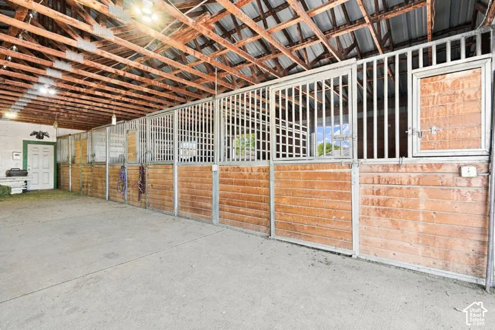 Barn interior featuring multiple stalls with wood paneling and metal grates, exposed wood beam ceiling, and concrete flooring