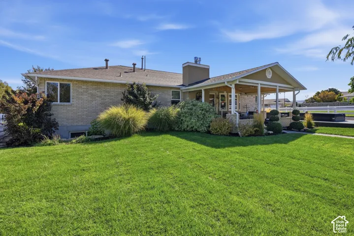 Expansive green lawn with mature landscaping, covered patio with white columns, and brick exterior