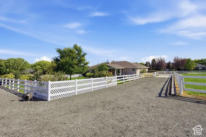 Gravel driveway bordered by white fencing, encompassing a large grassy area with mature trees and a single-story residence