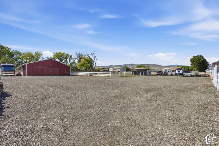Expansive gravel lot featuring a red barn with double doors and a white fence enclosure