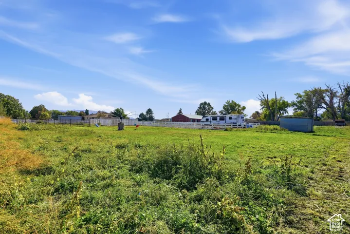 Expansive grassy field with perimeter fencing, a distant red barn, and established trees