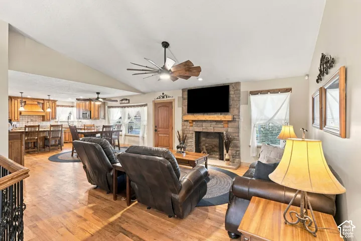 Vaulted ceiling, wood-finish flooring, stone-clad fireplace, wood cabinetry, and a ceiling fan with integrated lighting