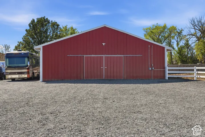 Red metal-sided barn with a white trim gable roof, large sliding barn doors, gravel ground cover, and a white fence