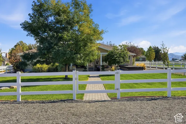 White three-rail fencing enclosing a manicured lawn, paver pathway, and mature trees