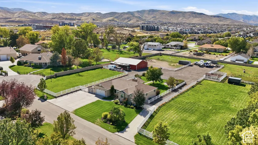 Expansive property featuring a large house with an attached garage, a red barn, a gravel-surfaced area, and multiple fenced grassy sections