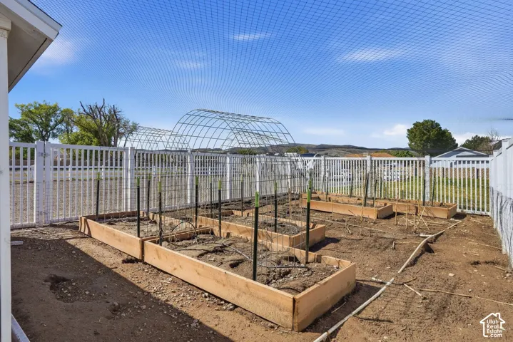 Expansive garden area featuring multiple raised beds, a white picket fence, a protective mesh canopy, and metal hoop structures