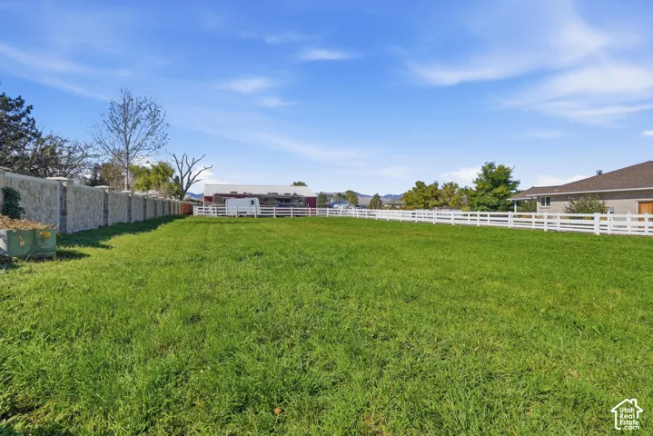 Expansive grass lawn with a white fence border and a stone-clad wall