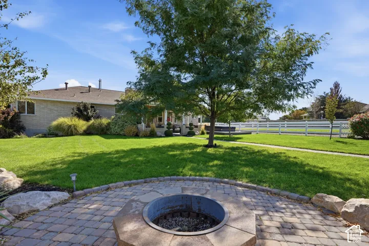 Brick exterior, paver patio, built-in fire pit, manicured lawn, and white fencing