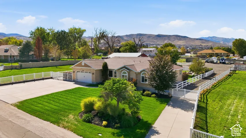 Expansive green lawn, mature trees, concrete driveway, white fencing, and an attached garage with a paved apron