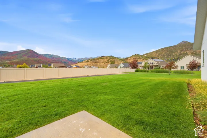 Expansive lawn area with a concrete pad, surrounded by a light-colored privacy fence and distant mountains