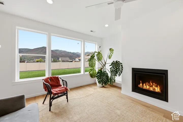 Spacious room featuring multiple large windows, a built-in fireplace, wood-finish flooring, recessed lighting, and a ceiling fan