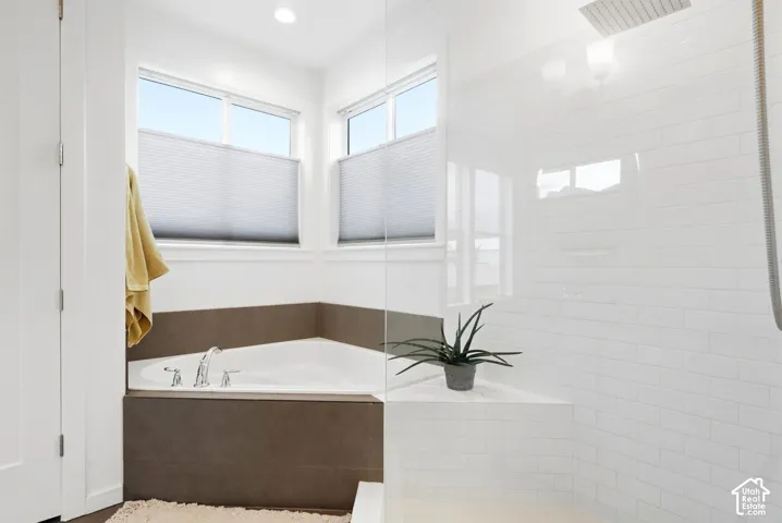 Corner soaking tub with polished chrome fixtures, white subway tile shower, and dual windows with privacy blinds