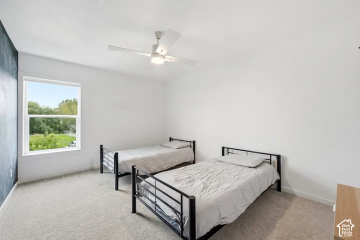 Spacious room with plush carpeting, a large window, a modern ceiling fan, and crisp white walls