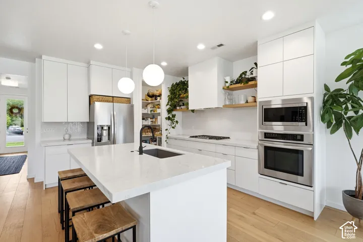 White shaker cabinetry with integrated stainless steel appliances, a large central island with seating, a built-in cooktop, and wood-finish flooring