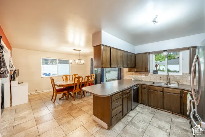 Kitchen and dining area featuring tile flooring, wood-finish cabinetry, a tile backsplash, and a double-basin stainless steel sink