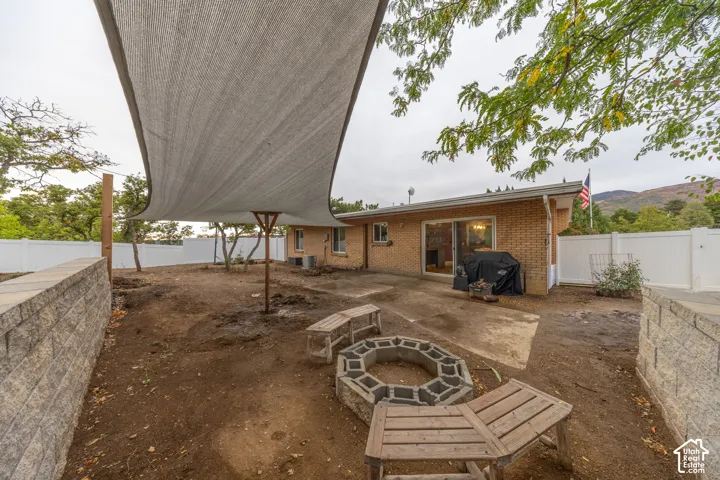 Expansive backyard featuring a partial shade structure, brick exterior, sliding glass door, and a built-in stone fire pit