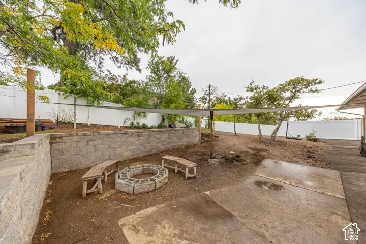 Stone block retaining wall, concrete patio area, built-in fire pit, privacy fencing, mature trees