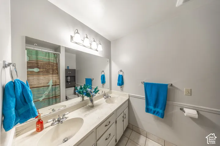 Dual vanity with integrated sinks, expansive mirror, wall-mounted light fixture, and tile flooring