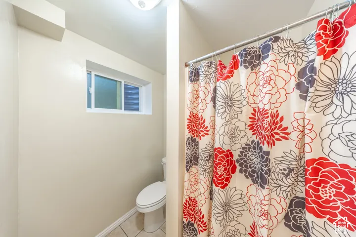 Compact bathroom featuring a white toilet, tile flooring, and a sliding window