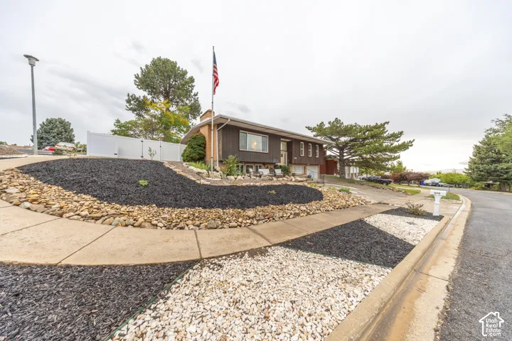 Tiered landscaping featuring decorative rock and mulch, a concrete sidewalk, and a white privacy fence