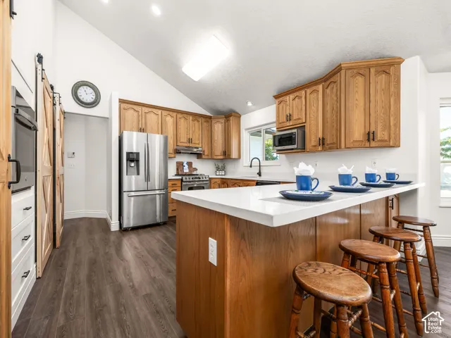 Kitchen featuring wood cabinetry, stainless steel appliances, a white island countertop, wood-finish flooring, and vaulted ceilings