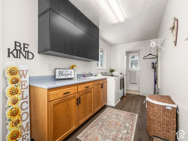 Laundry room with wood-finish flooring, light wood-finish lower cabinetry, dark upper cabinetry, and a light-toned countertop