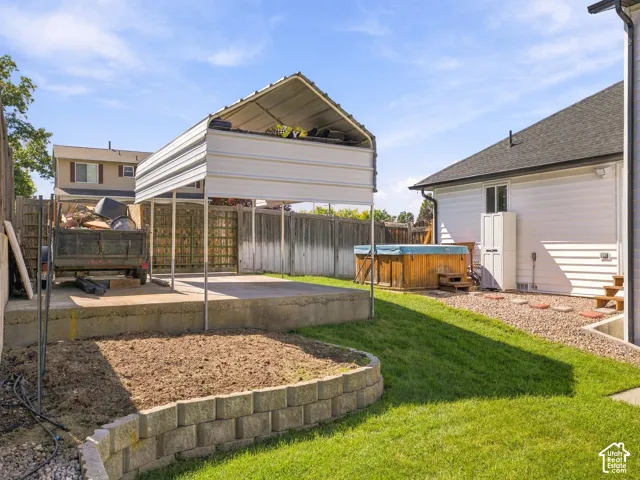 Expansive backyard featuring a manicured lawn, block retaining wall, and a raised patio with a carport structure