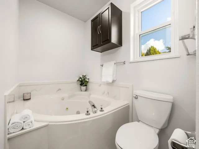 Corner jetted tub with polished chrome fixtures, white tile surround, and an upper window