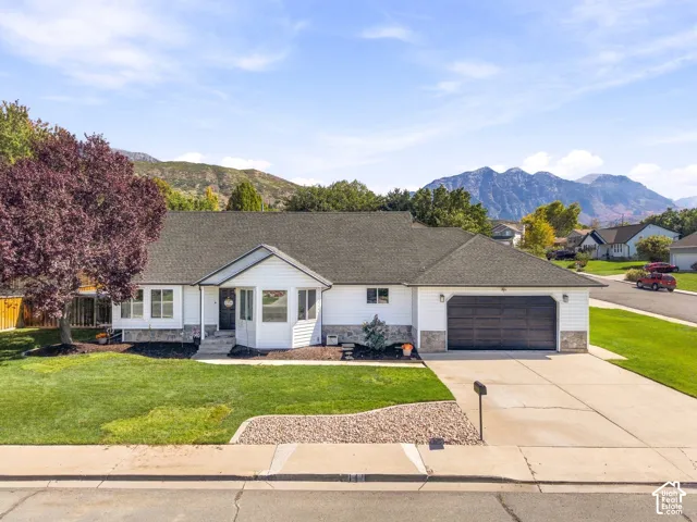 White siding exterior with a dark shingle roof, stone accent detailing, an attached two-car garage, and a concrete driveway