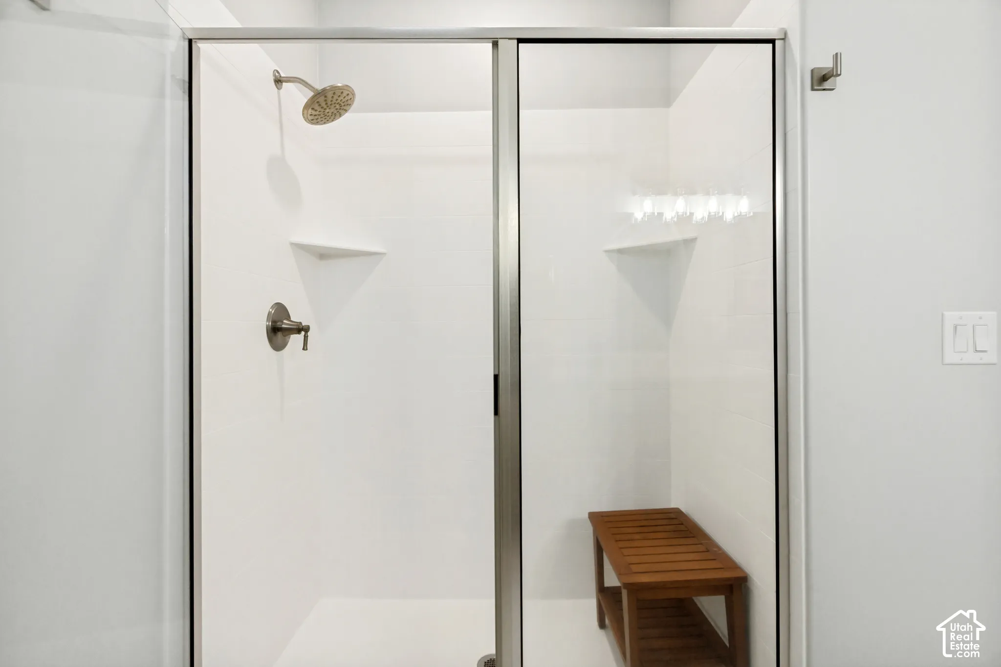 Glass-enclosed shower with brushed nickel fixtures, a rain showerhead, and a built-in corner shelf