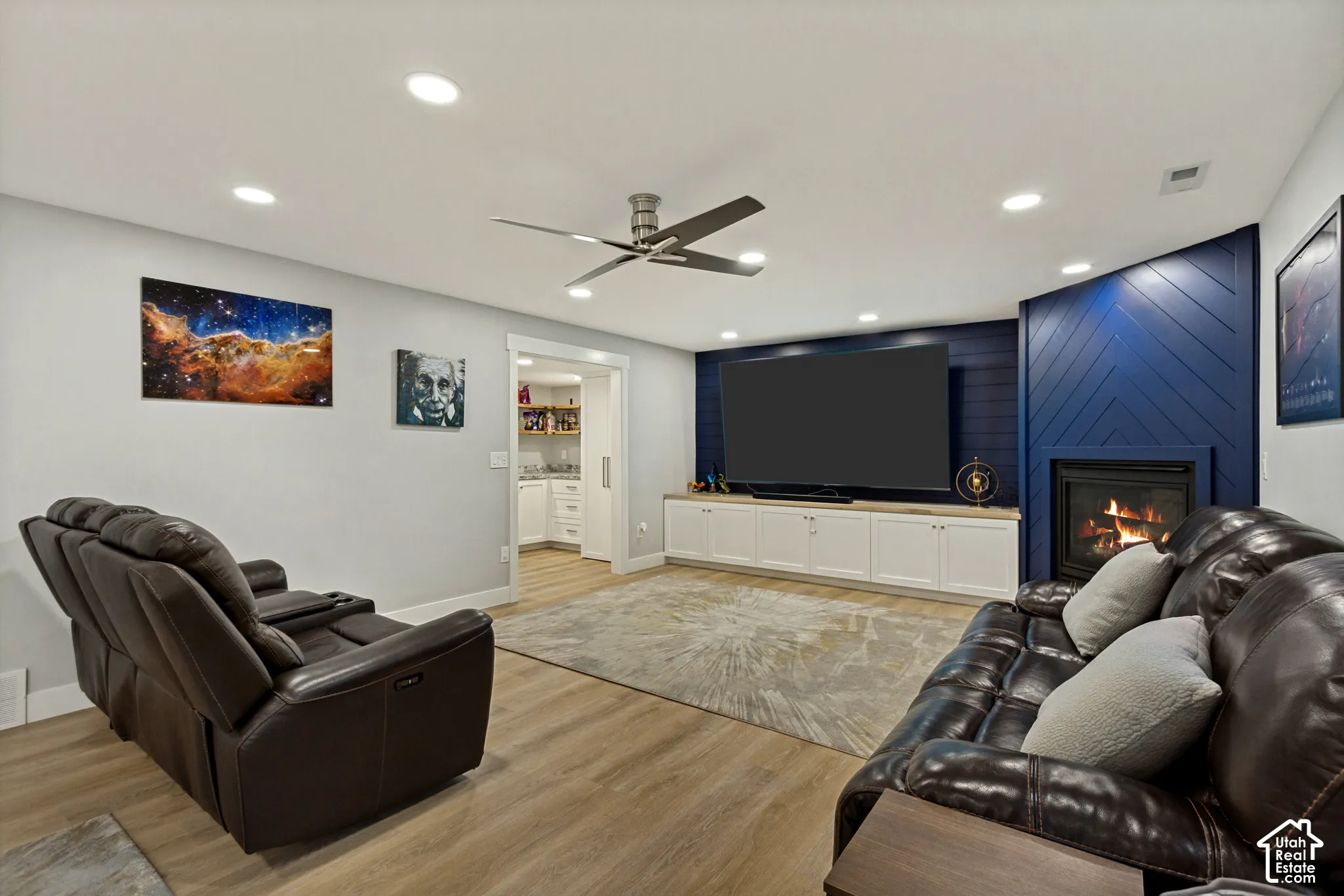 Recessed lighting throughout, LVP flooring, built-in media console with storage, modern fireplace with blue paneling, and a ceiling fan