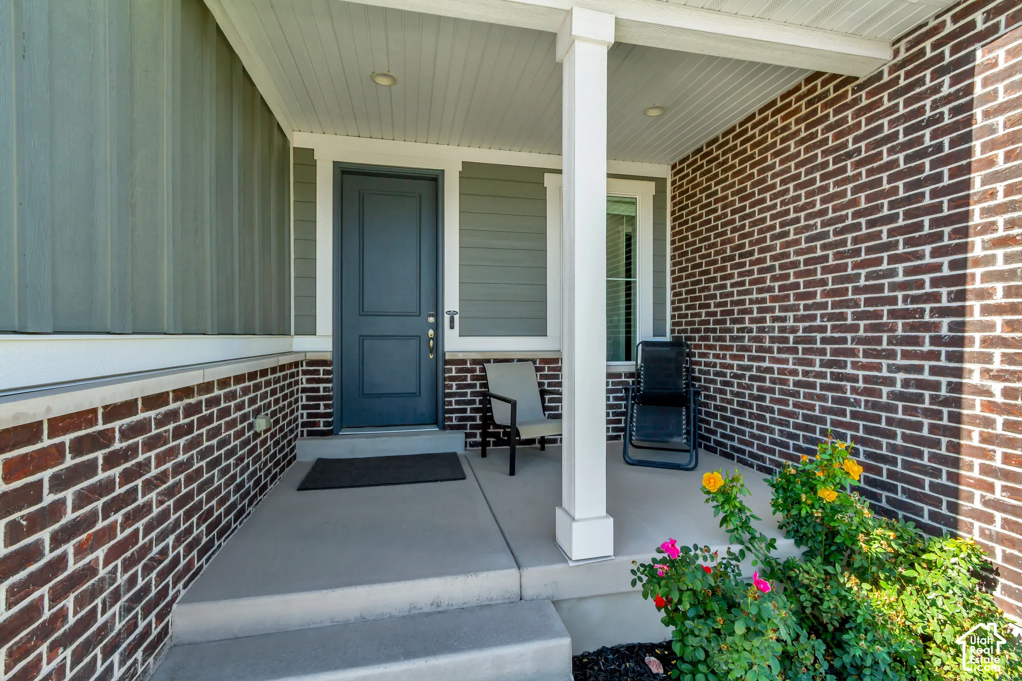 Covered front porch featuring brick and siding exterior, concrete steps, a paneled front door, and a built-in light fixture