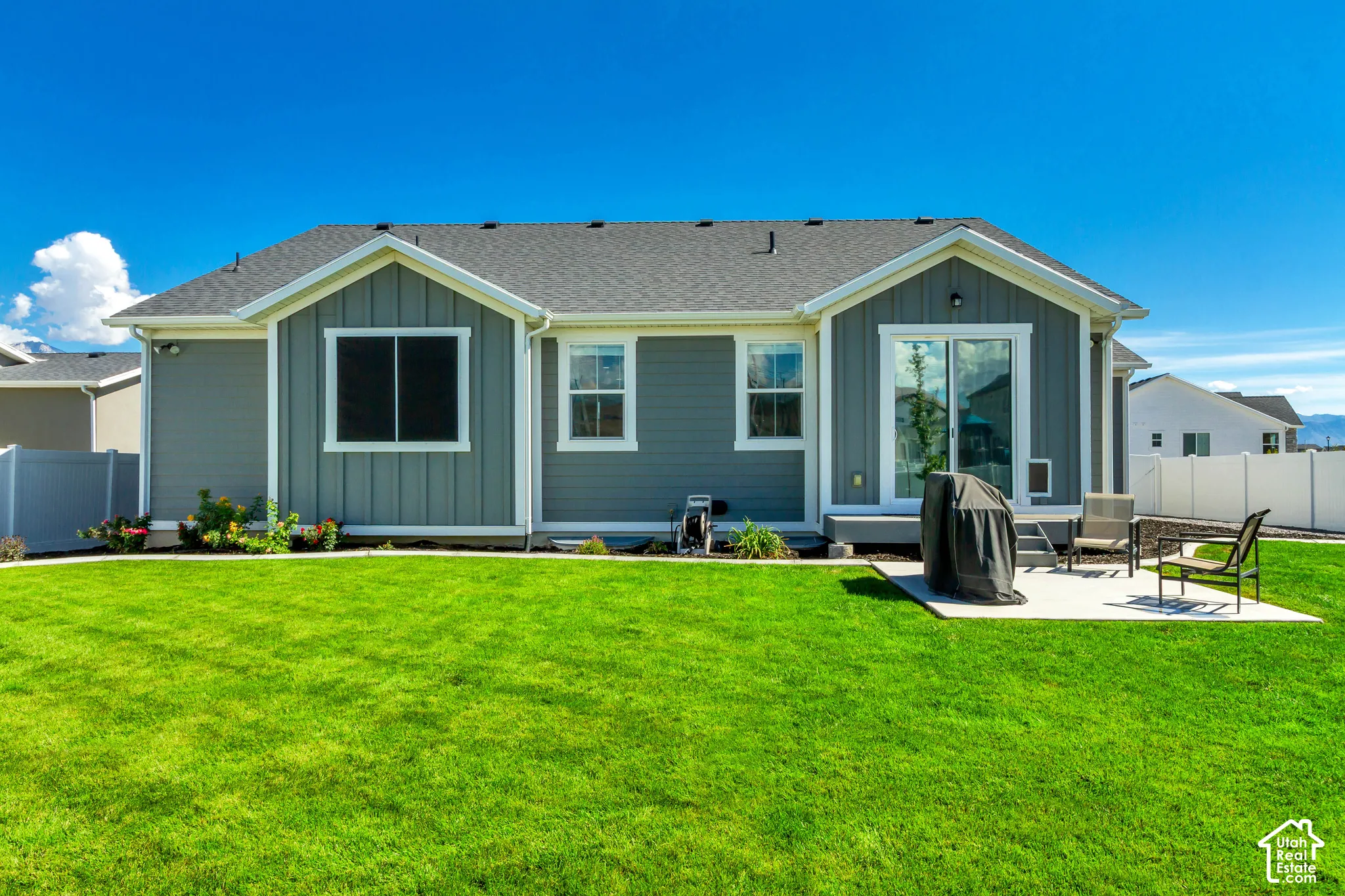 Expansive green lawn, exterior featuring horizontal and vertical siding, white trim, sliding glass door, and a concrete patio