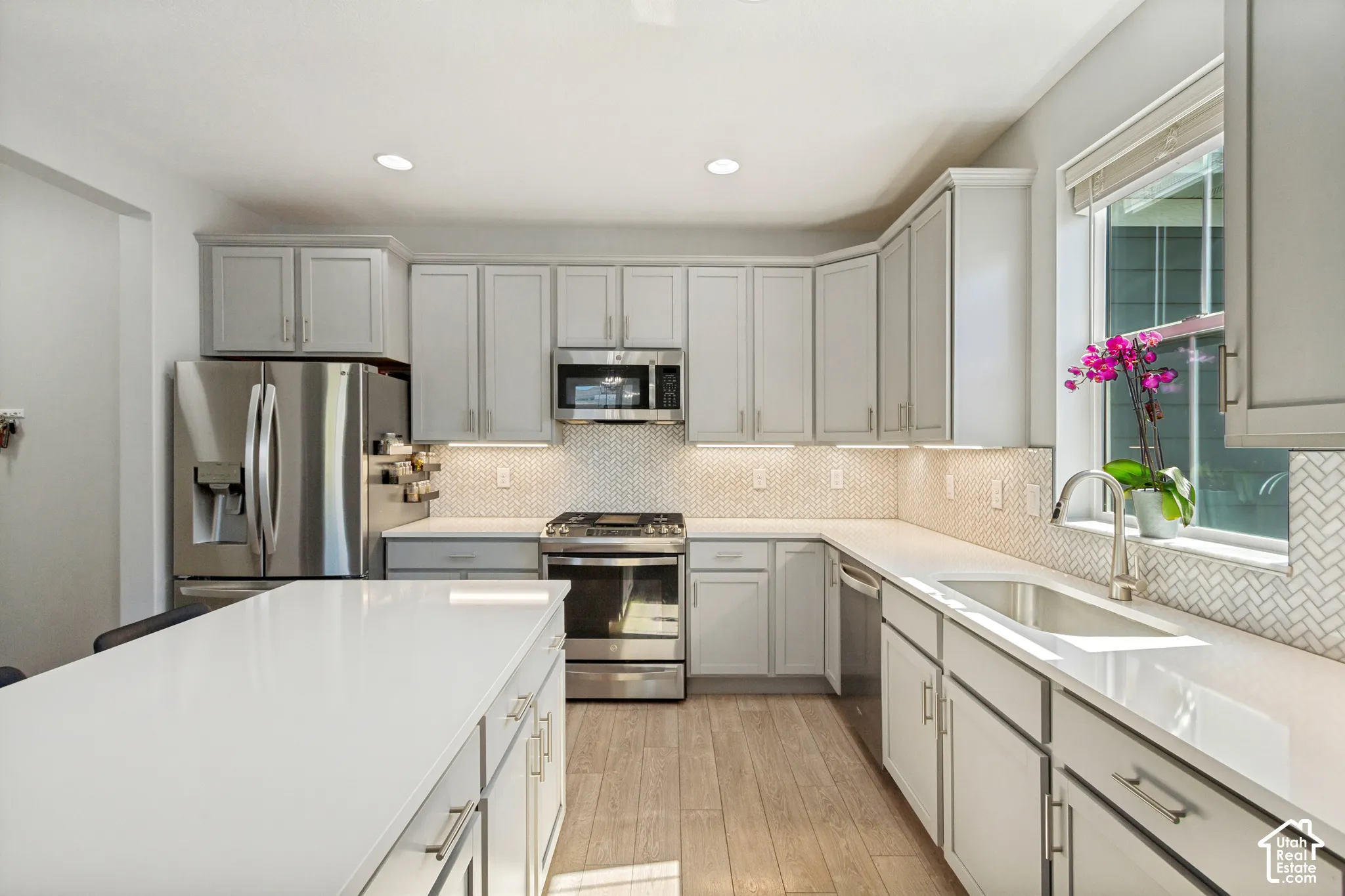 Contemporary kitchen featuring light gray cabinetry, stainless steel appliances, white countertops, and a full tile backsplash