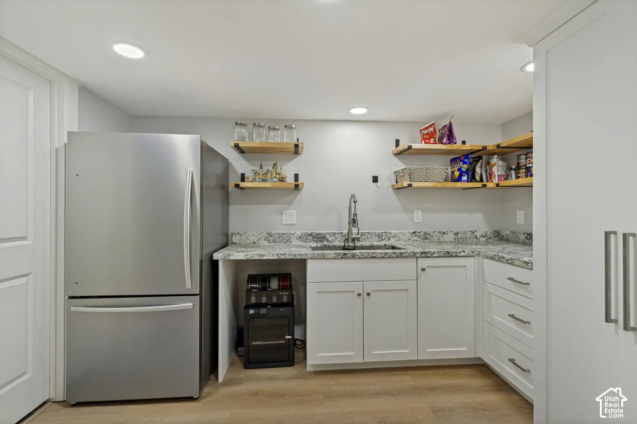 Kitchenette featuring white cabinetry, granite-style countertops, stainless steel sink, and open wood shelving