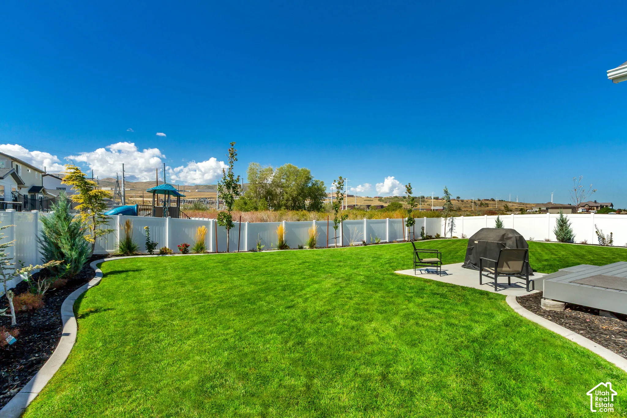 Expansive backyard featuring a manicured lawn, white privacy fencing, and a concrete patio