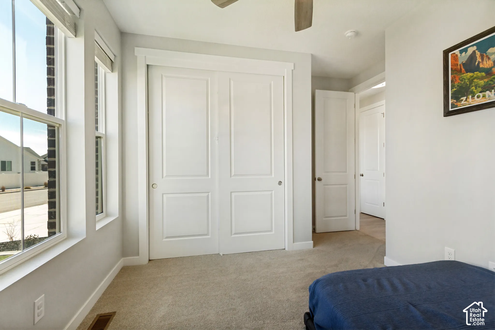 Dual pane windows, white paneled bifold closet doors, light neutral carpeting, and a ceiling fan
