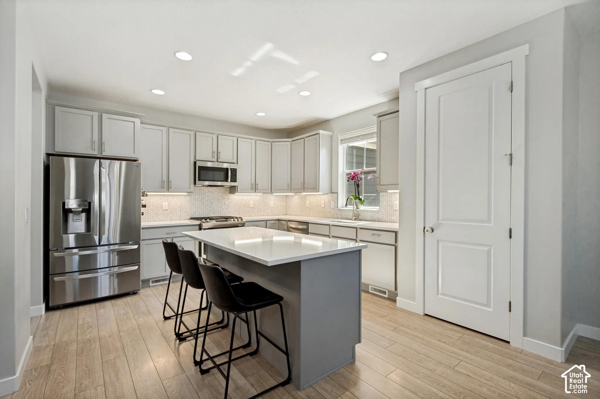 Kitchen featuring light gray cabinetry, stainless steel appliances, a white quartz countertop island, white tile backsplash, and LVP flooring